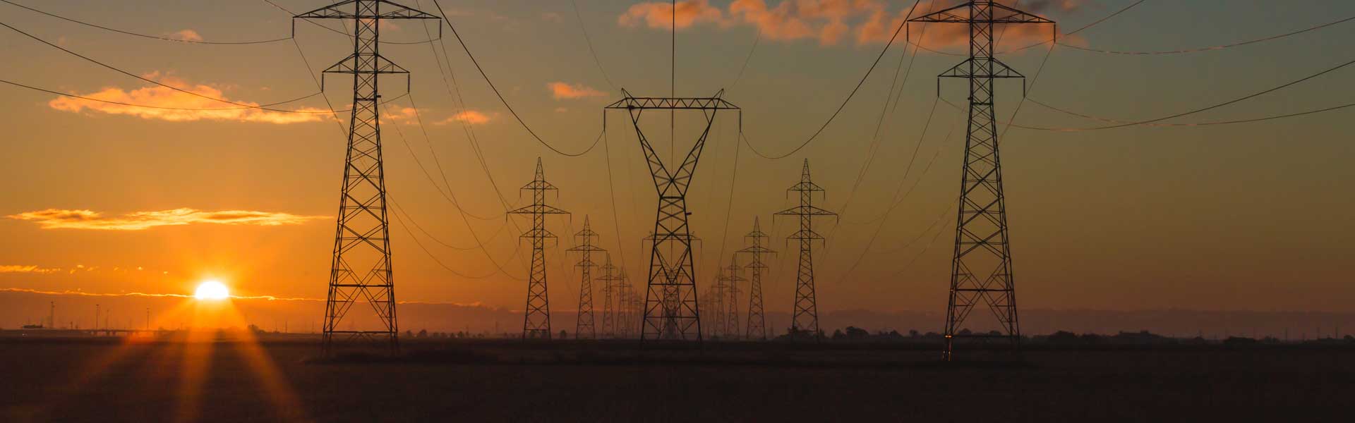 Power lines heading into a horizon with a setting sun.