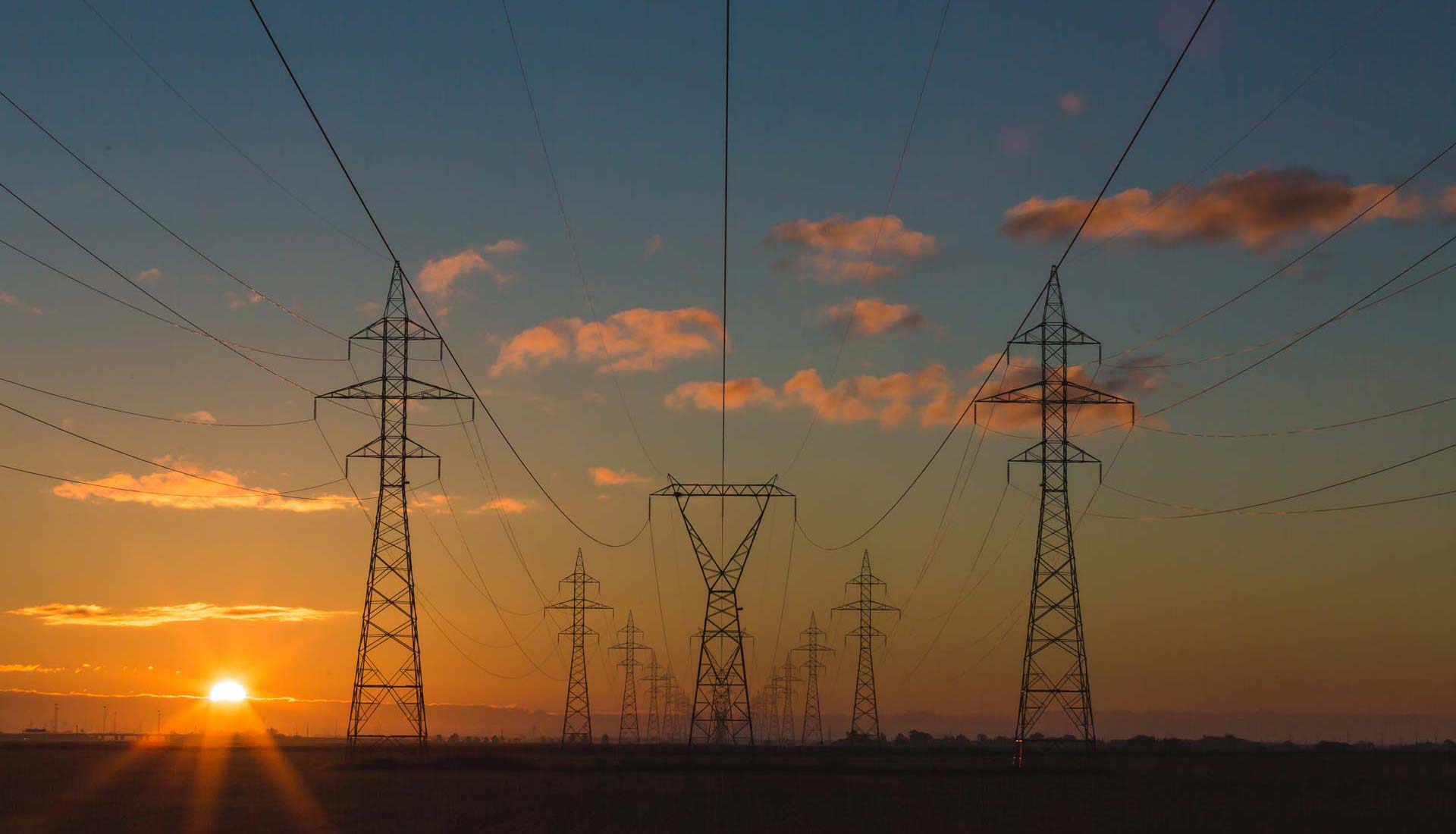 Power lines heading into a horizon with a setting sun.