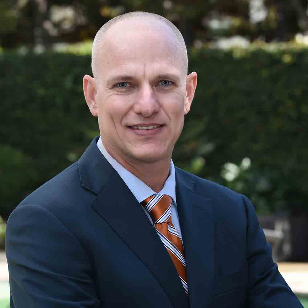 Profile picture of man wearing blue suit with orange and blue striped tie.